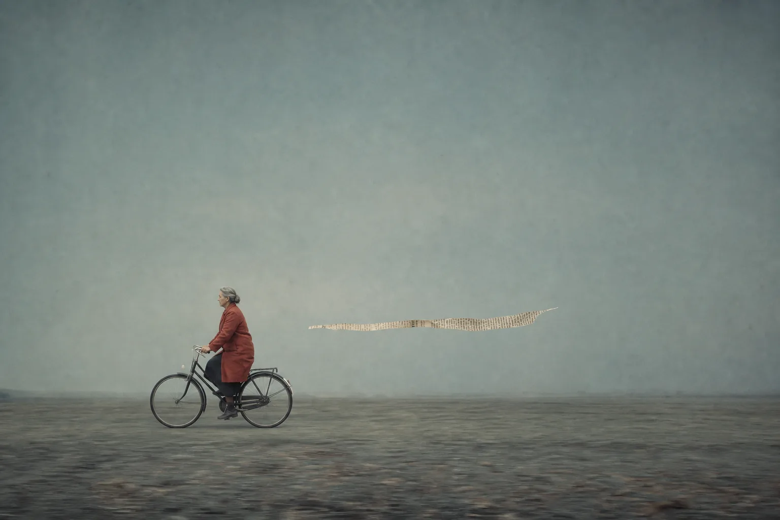 An older woman riding a bicycle beside a narrow archival fragment