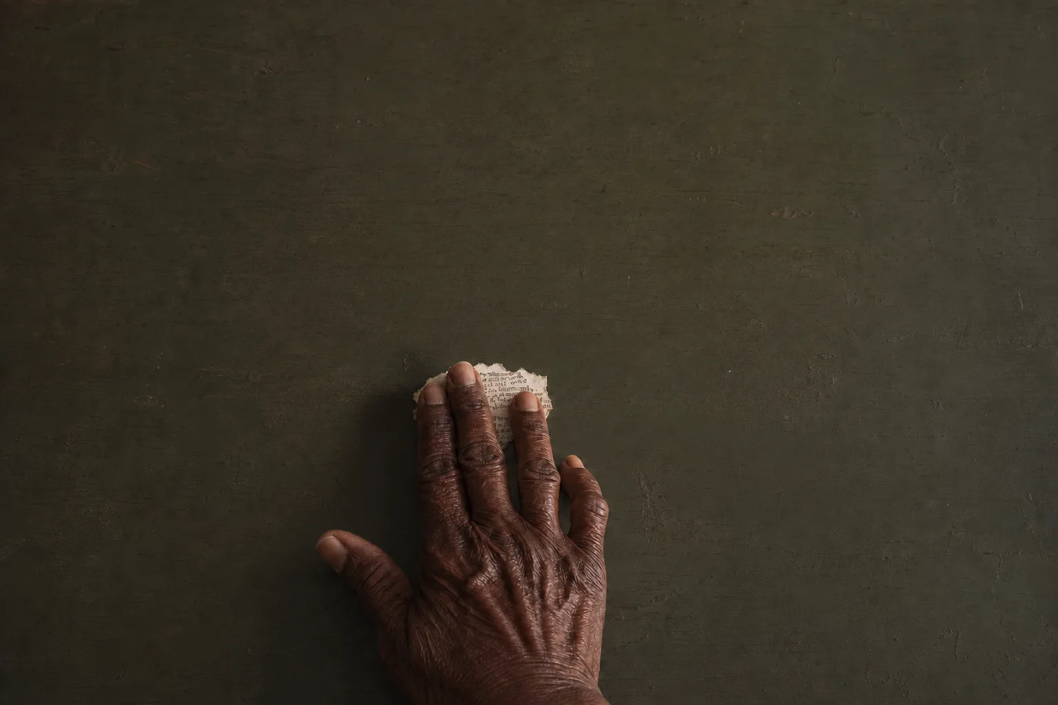 An older hand resting over a small archival fragment